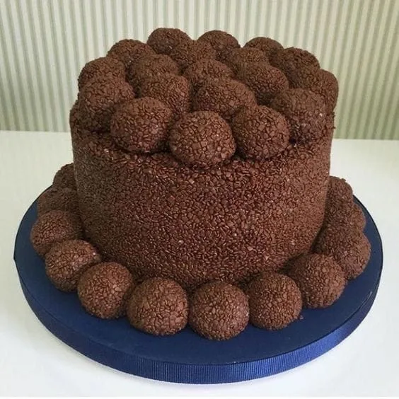 Bolo de chocolate coberto de granulado, com brigadeiros em volta